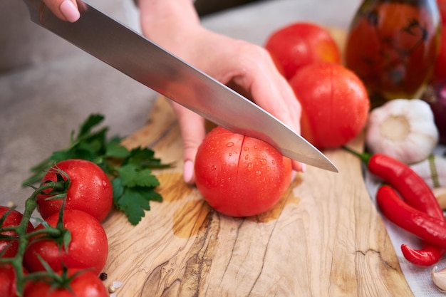 Femme faisant une encoche sur une tomate sur une planche à découper en bois sur une table en béton ou en pierre de cuisine grise