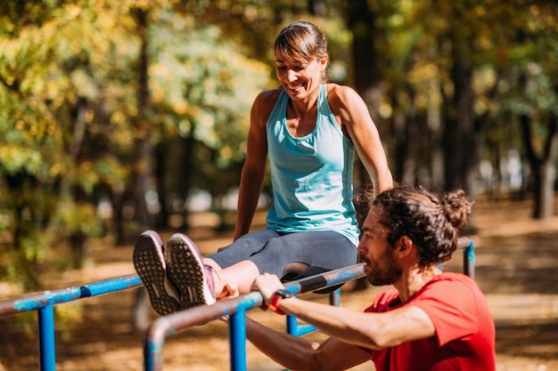 Femme faisant de l'exercice sur une barre parallèle dans le parc avec un entraîneur personnel