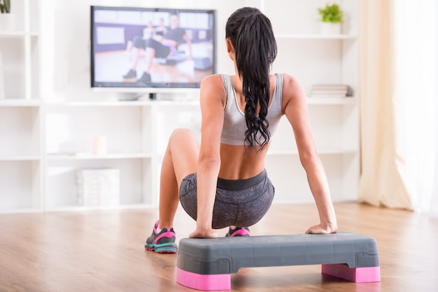 Femme faisant des exercices à la maison tout en regardant le programme.