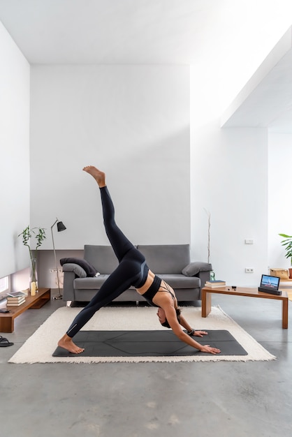 Femme faisant une jambe vers le bas face à un chien fendu à l'aide d'un programme de formation de yoga en ligne sur la tablette