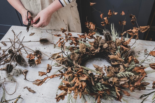 Photo femme faisant une petite couronne d'hiver de plantes séchées feuilles brunes et brindilles et graines
