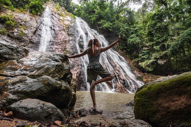 Femme faisant une posture de yoga devant une cascade entourée de végétation Vacances d'été