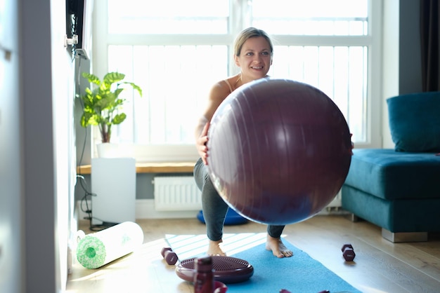 Femme faisant des squats avec un ballon bordeaux à la maison