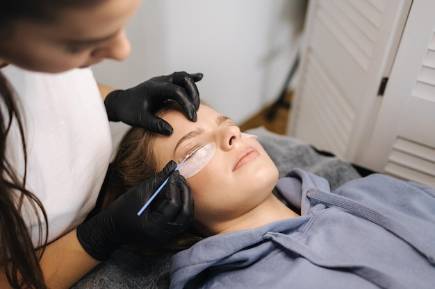 Femme faisant la stratification des cils dans le modèle de cheveux blonds de studio de beauté a la stratification de curling de coloration