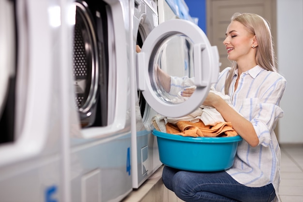 Femme faisant les tâches quotidiennes - lessive. Femme vêtements propres pliés dans le lavabo, vue latérale sur femme appréciant le processus de nettoyage dans la maison de lavage. nettoyage, concept de lavage