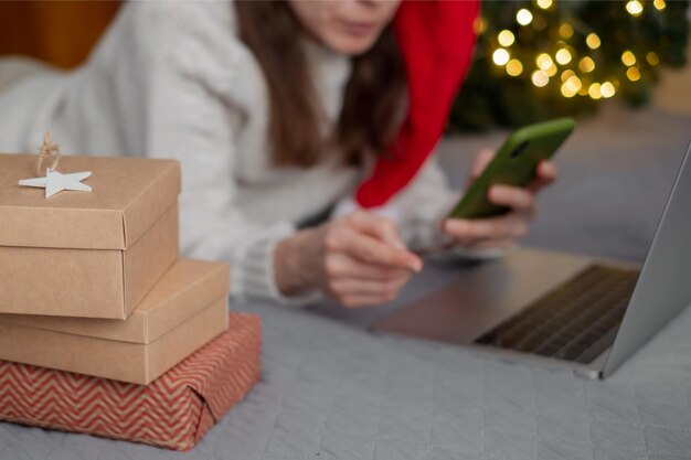 Une femme fait des achats de Noël en ligne avec un ordinateur portable sur fond de lumières de Noël