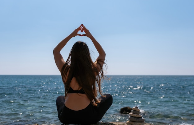 Femme fait coeur avec les mains sur la plage jeune femme avec instructeur de fitness cheveux longs qui s'étend