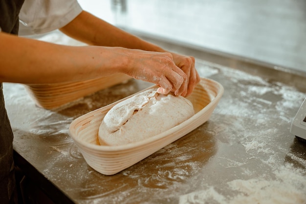 Une femme fait un décor sur du pain cru dans un plat en céramique dans une boulangerie artisanale