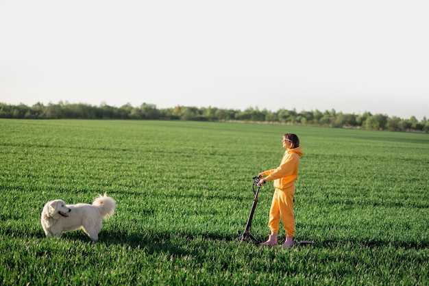 Une femme fait du scooter électrique sur un champ vert avec un chien