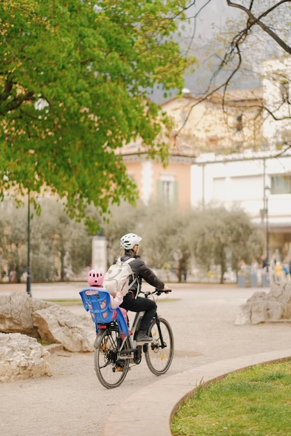 Une femme fait du vélo avec un enfant sur le dos.