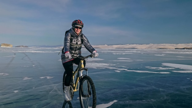 La femme fait du vélo sur la glace La fille est vêtue d'un sac à dos et d'un casque de vélo en duvet argenté La glace du lac Baïkal gelé Les pneus à vélo sont recouverts de pointes