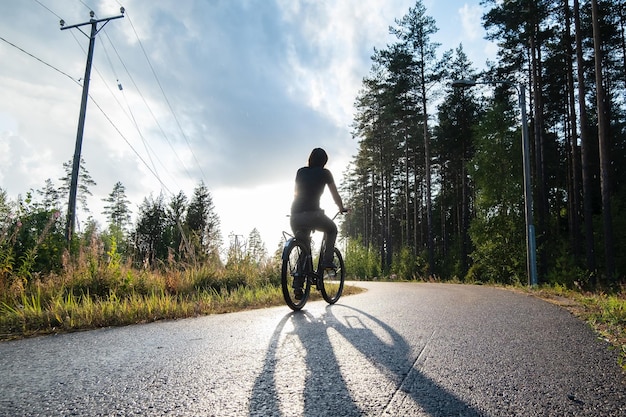 Une femme fait du vélo sur une piste cyclable près d'une pinède et profite d'une chaude soirée