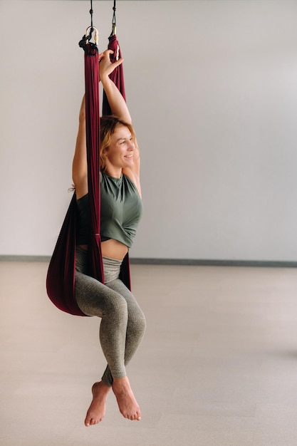 Une femme fait du yoga assise dans un hamac suspendu dans la salle de sport.