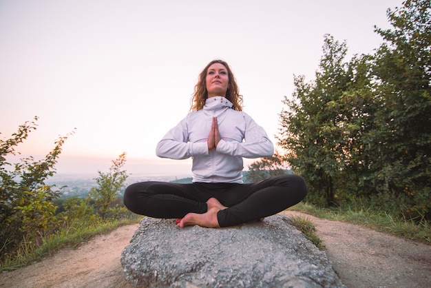 Une femme fait des exercices de yoga au sommet de la colline au lever du soleil