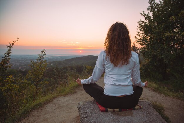 Une femme fait des exercices de yoga au sommet de la colline au lever du soleil