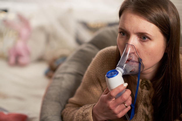 Femme fait nébuliseur d'inhalation à la maison. tenant un nébuliseur de masque inhalant des vapeurs vaporisez le médicament dans vos poumons, malade du patient.