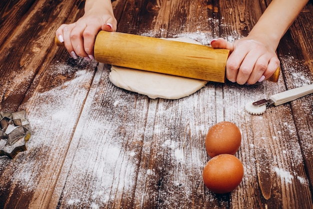 Femme fait des pâtisseries de Noël sur la pâte sur une table en bois