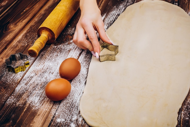 Femme fait des pâtisseries de Noël sur la pâte sur une table en bois