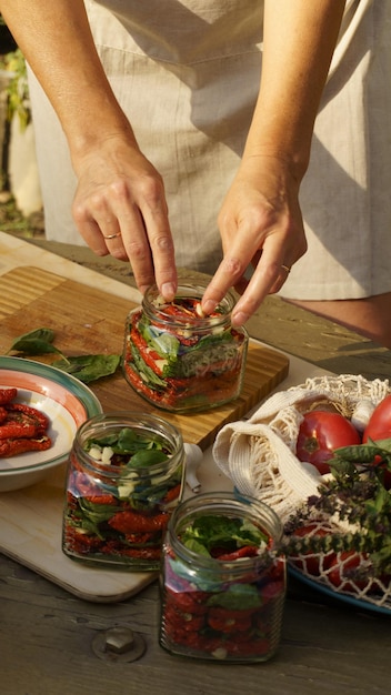 une femme fait des préparations pour les tomates séchées d'hiver, l'ail haché et le basilic frais sont mis en bocaux