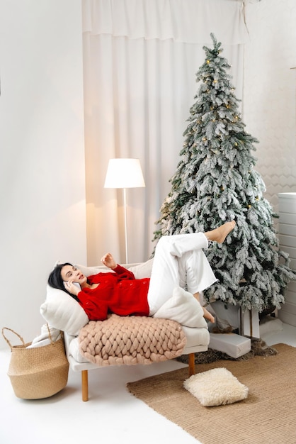 Une femme fait ses achats de Noël en ligne, elle est assise sur le canapé à la maison et parle au livreur