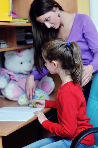 femme de famille heureuse et fille travaillant sur leurs devoirs à la maison pendant que maman montre le globe et donne de l'aide