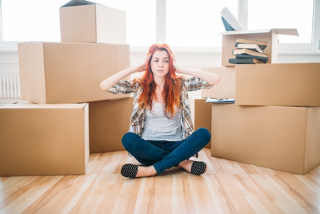 Femme fatiguée assise dans la pose d'yoga parmi les boîtes en carton, pendaison de crémaillère. Déménagement dans une nouvelle maison