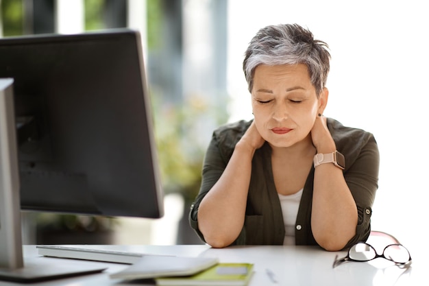 Femme fatiguée assise sur le lieu de travail, les yeux fermés, se frottant le cou