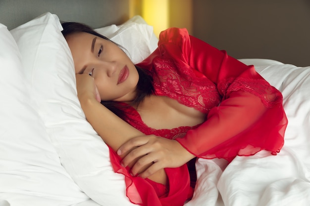 Une femme fatiguée couchée dans son lit ne peut pas dormir tard dans la nuit avec de l'insomnie. Fille asiatique portait une chemise de nuit en satin et une robe rouge allongée sur le lit éveillé dans la chambre