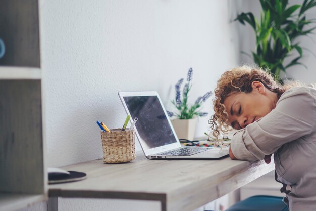 Photo femme fatiguée endormie devant un ordinateur portable à la maison dans la salle de travail du bureau. des femmes adultes dormant pour une activité de surmenage. concept de travail intelligent de la maladie moderne