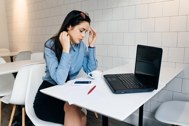 Une femme fatiguée est assise au bureau à table et boit du café