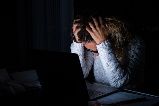 Femme fatiguée et frustrée travaillant et utilisant un ordinateur portable tard dans la nuit. Femme d'affaires contrariée d'avoir trop de travail