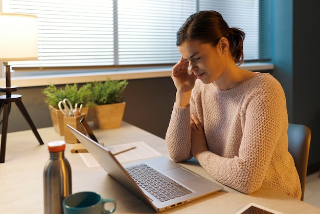 Femme fatiguée avec des maux de tête travaillant avec un ordinateur portable