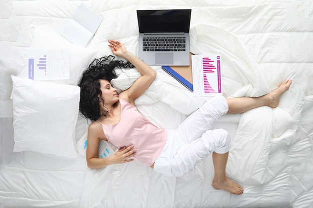 Femme fatiguée en pyjama dormir dans la pose dans un lit blanc.