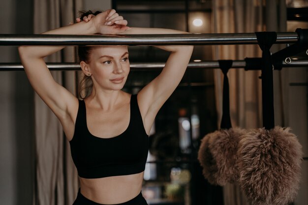 Femme fatiguée rousse en tenue de sport en pose de loisirs en détournant les yeux s'appuyant sur le cadre du réformateur cadillac dans la salle de sport se reposant après l'entraînement pilates dans un studio de fitness Mode de vie sain et sportifs