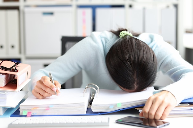 Une femme fatiguée se trouve sur un dossier avec des documents sur la table dans le concept d'heures supplémentaires et de date limite