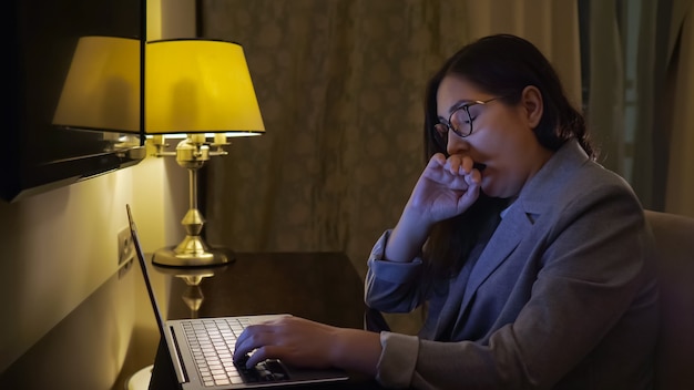 Femme fatiguée tapant sur un ordinateur portable à la lumière d'une lampe de table