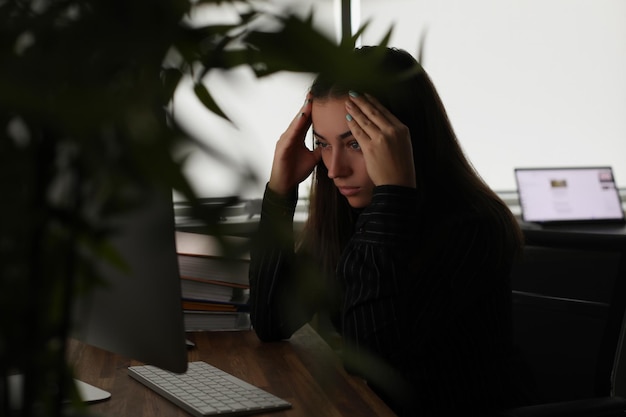 Femme fatiguée tenant sa tête avec les mains devant l'écran de l'ordinateur au bureau