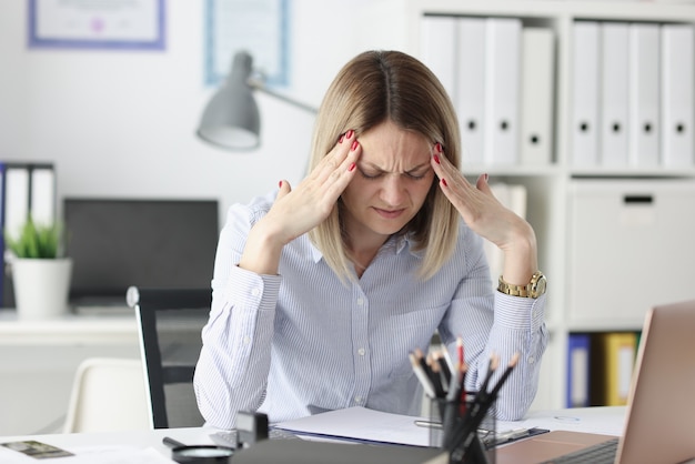 Femme fatiguée tient ses doigts sur ses tempes à la table de travail. Concept de journée de travail irrégulière
