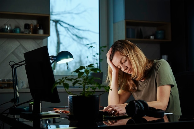 Une femme fatiguée travaille tard sur son lieu de travail à domicile la nuit