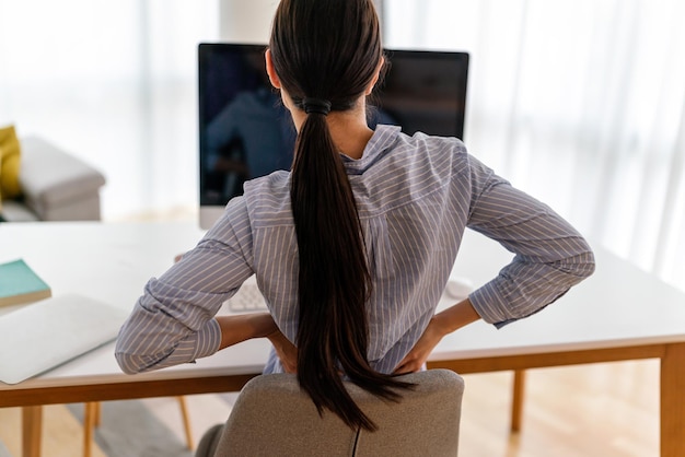 Femme fatiguée travailleuse assise à son bureau touche le dos souffre femme forte maux de dos concept de posture incorrecte
