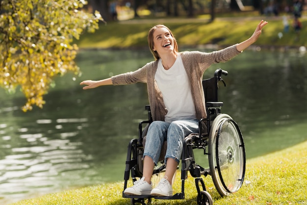Une femme en fauteuil roulant est assise au bord d'un lac.