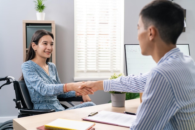 Une femme en fauteuil roulant est assise au bureau du bureau en face de son employeur et tient la main