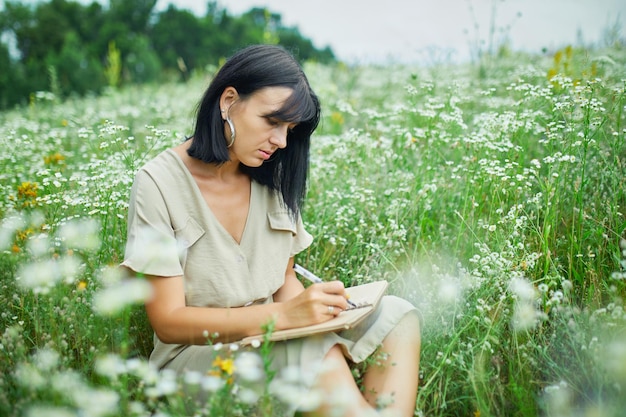 Femme femme avec stylo écrit ou peinture écriture manuscrite sur ordinateur portable sur une prairie en fleurs de fleurs