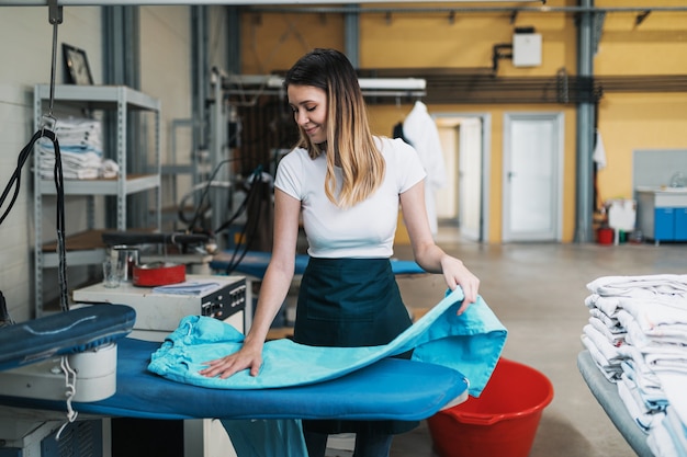 Femme avec fer travaillant à l'atelier de repassage. Services de nettoyage.