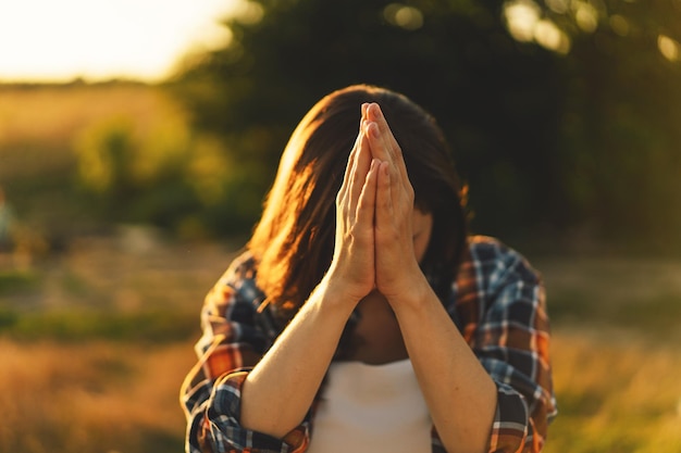 Une femme a fermé les yeux en priant dans un champ pendant un beau coucher de soleil