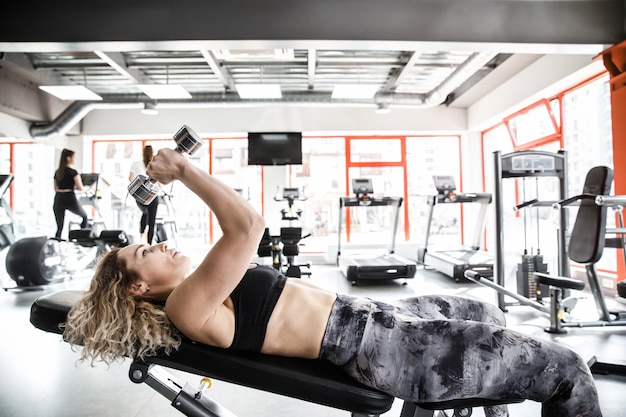 Une femme fille est allongée sur un appareil d'entraînement avec ses mains en l'air. Elle fait de l'exercice avec un haltère