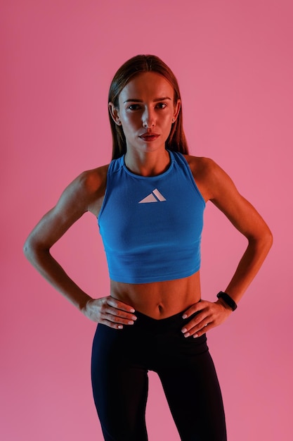 Une femme de fitness attrayante portant des vêtements de sport posant sur le fond du studio et regardant la caméra