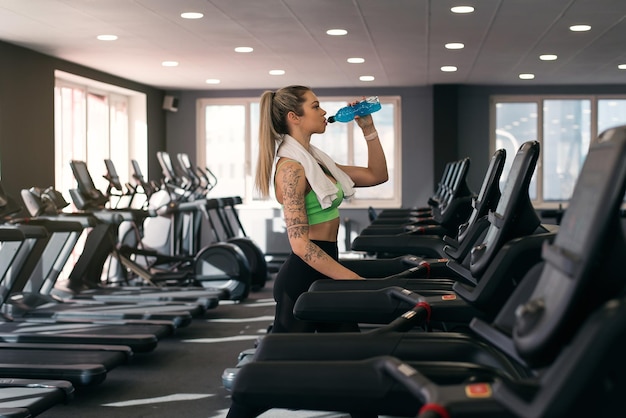 Une femme de fitness buvant de l'eau en faisant de l'exercice sur un tapis roulant au gymnase