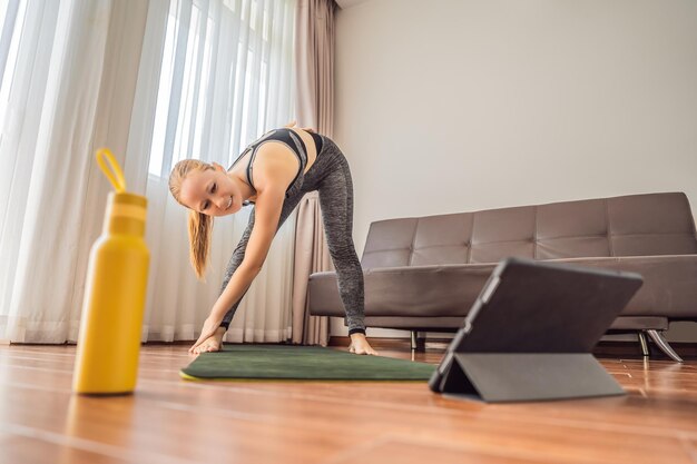 Une femme de fitness faisant de l'exercice sur le sol à la maison et regardant des vidéos de fitness sur une tablette que les gens font