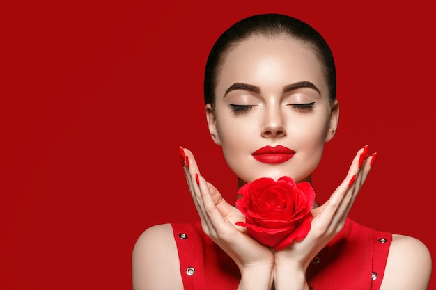 Femme avec fleur rose. Portrait féminin de beauté avec de beaux ongles de manucure de fleur rose et coiffure de salon sur fond rouge